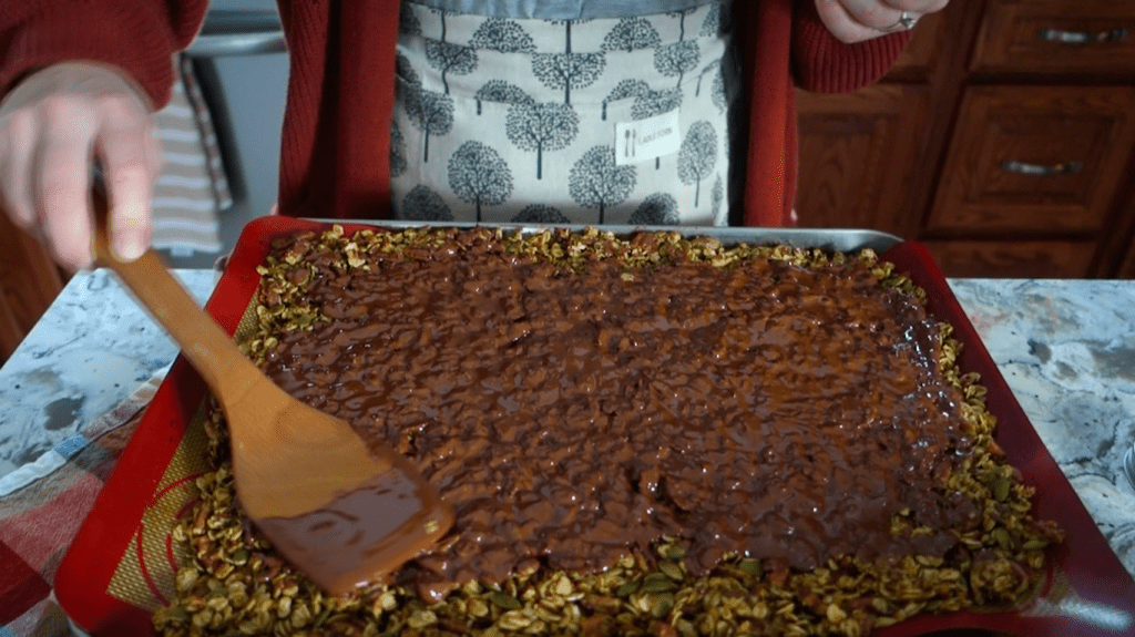 spreading chocolate in an even layer on top of granola