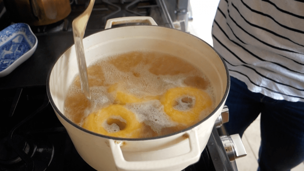placing homemade sourdough bagel dough into pot of boiling water in a white martha stewart dutch oven on a gas stove