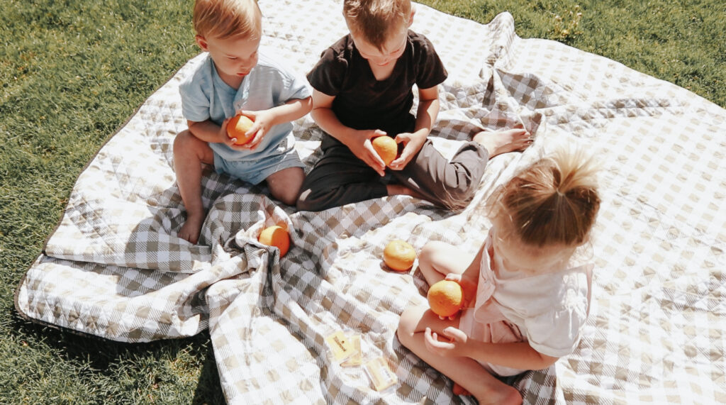 Three children play on a checkered green and white blanket.