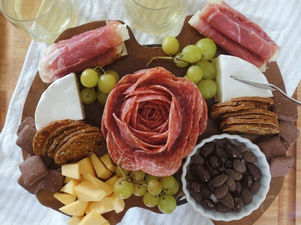 small charcuterie board with a salami rose in the center various meats and cheese options and two glasses on wine