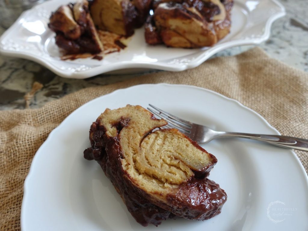 slice of sourdough babka on a white plate with two babka loaves in the background