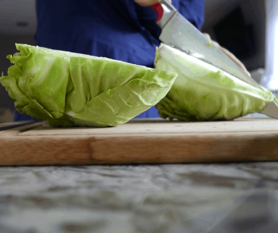 bright green cabbage cut in half on wooden cutting board using a chefs knife