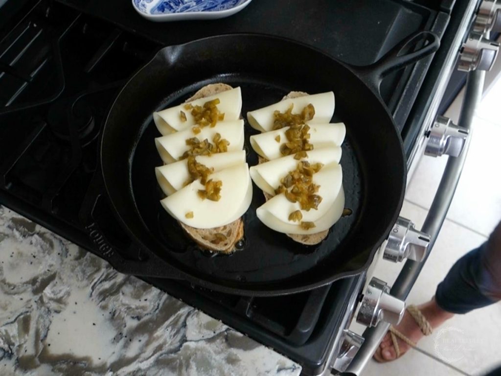 two slices of bread on a cast iron skillet with cheese and jalapenos on top showing how to make a grilled cheese without butter
