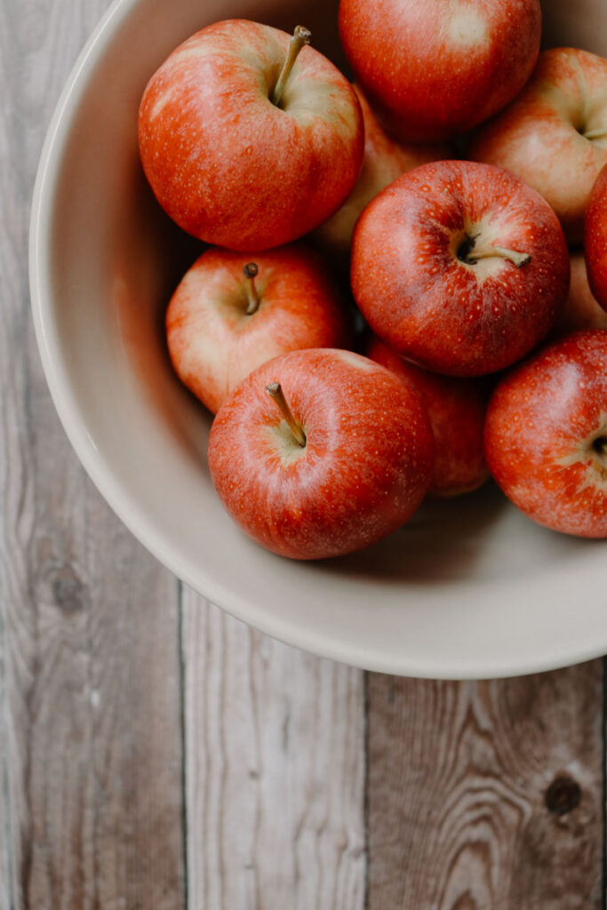 apples in a large bowl on a wooden table shown before making into homemade applesauce