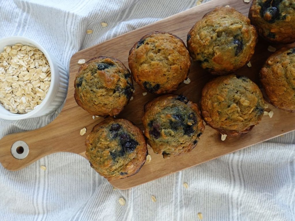 banana blueberry muffins on a wooden platter with a bowl of oats