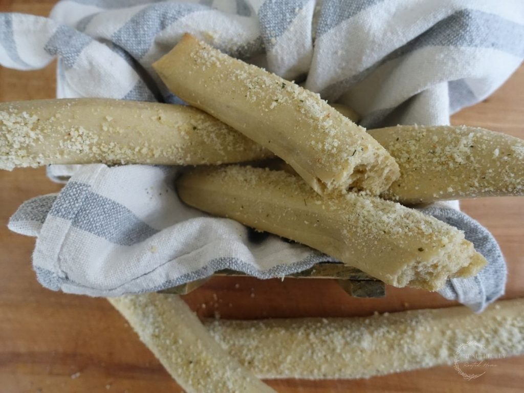 sourdough breadsticks stacked on top of each other in a box lined with a ticking stripe tea towel