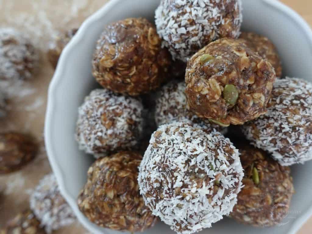 no bake boobie balls in a white bowl with half covered in coconut flakes and half not