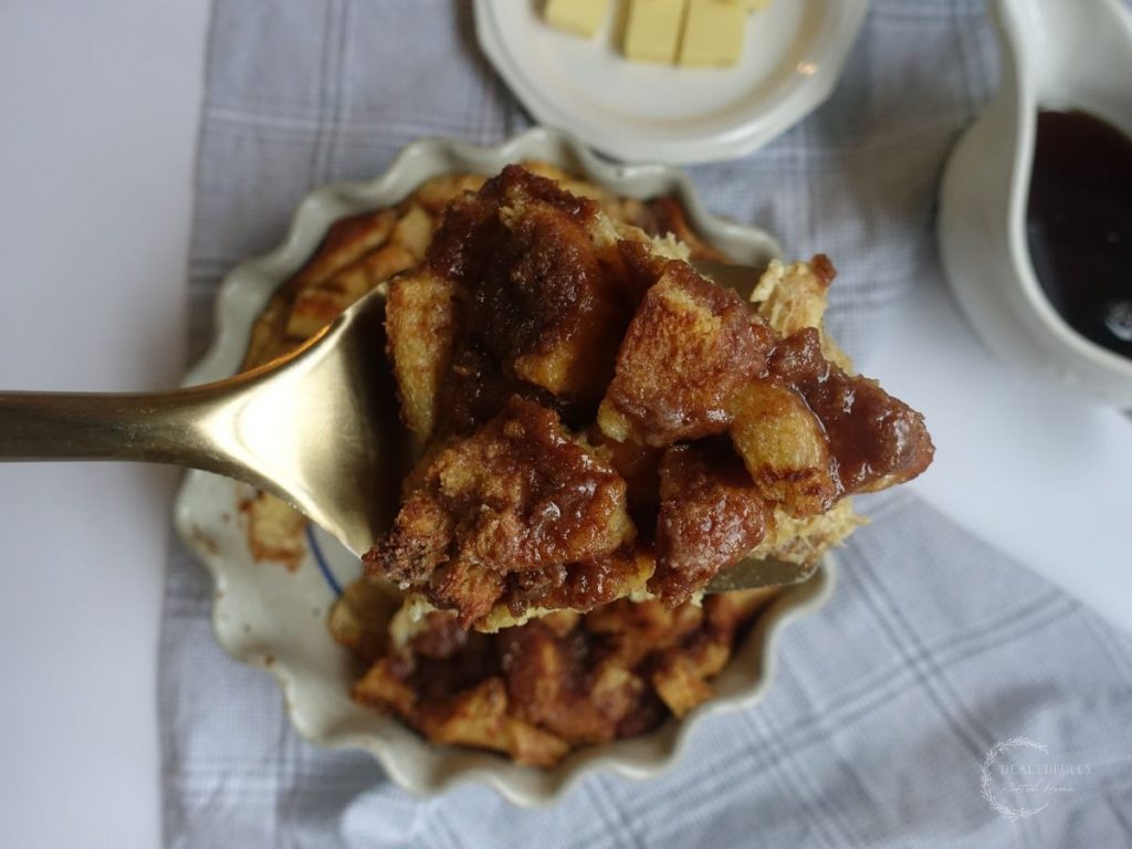 holding up a slice of brioche french toast casserole on a golden spatula above the dish with the entire casserole