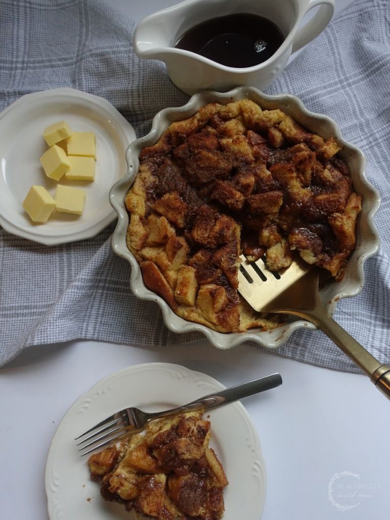 flat lay picture of brioche french toast casserole with a slice taken out and set on a plate with pads of butter and maple syrup