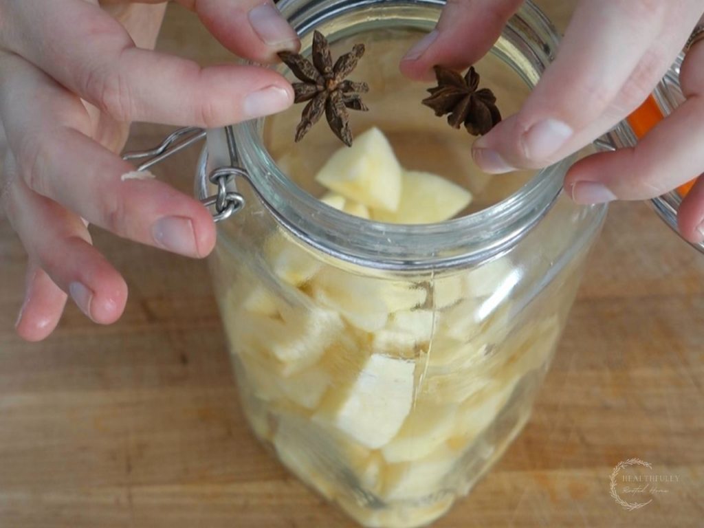 adding star anise to a jar of chopped and peeled apples for making fermented apples