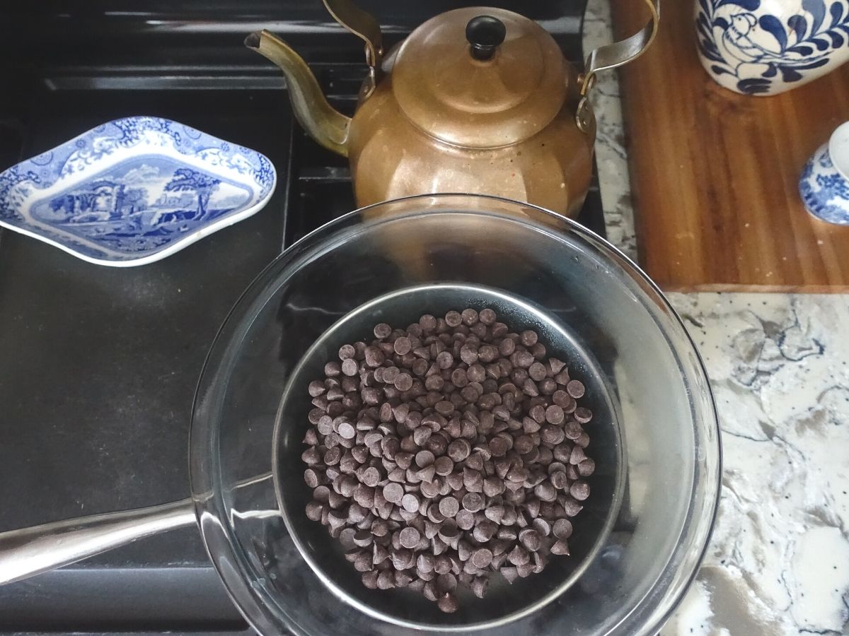 chocolate chips in a double broiler on the stove with a copper tea kettle behind it