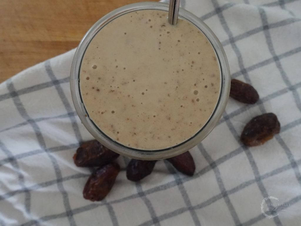 dates milkshake in a drinking glass with a stainless steel straw on a tea towel surrounded by dates