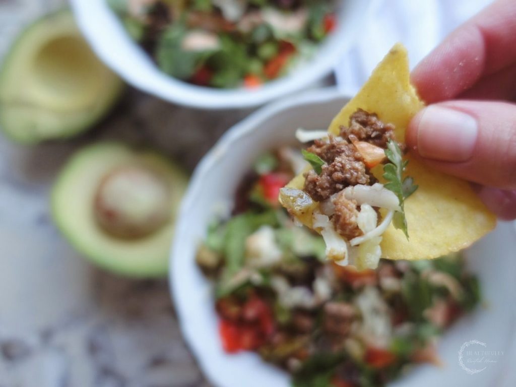 deconstructed tacos with tortilla chips dipped into them with avocado on the side