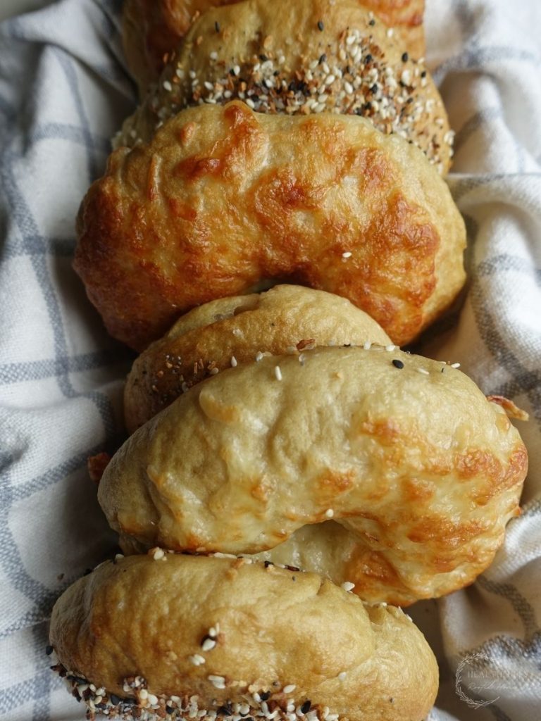 sourdough discard bagels lined up in a basket lined with a tea towel with each bagel having different toppings