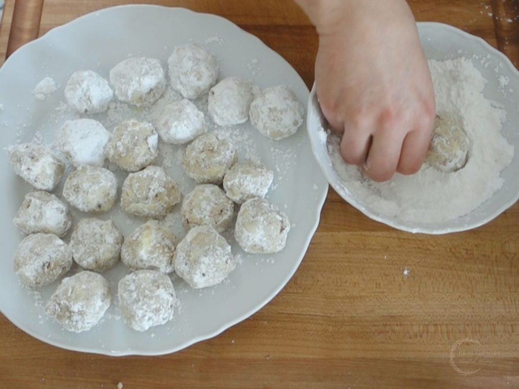 rolling pecan snowball cookies in powdered sugar then putting on a white plate