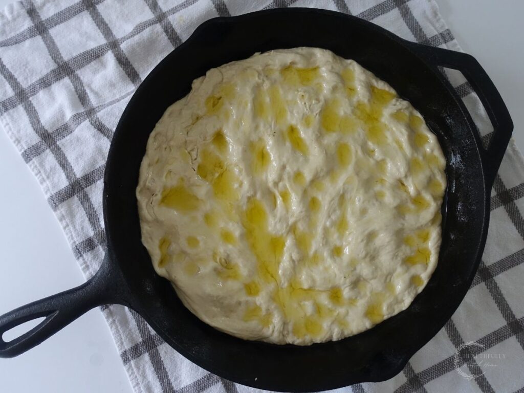 dough for sourdough discard focaccia in a cast iron skillet dimpled with olive oil drizzle
