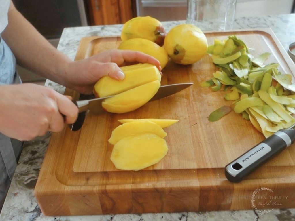dicing peeled mangos on a wooden boos block cutting board with other peeled mangos in the background