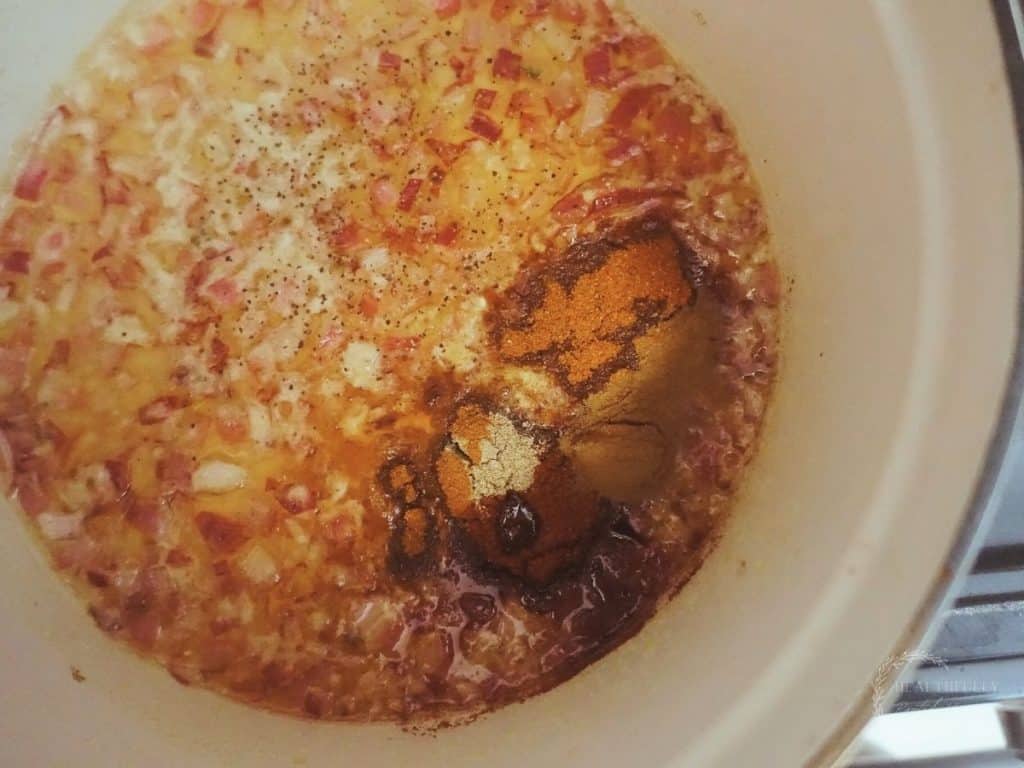 spices with sauteed onions in a white dutch oven with lots of bubbles