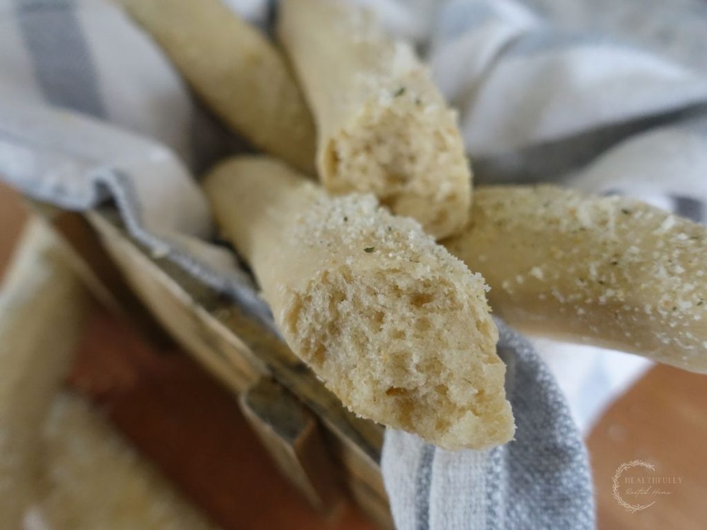 sourdough breadsticks on top of eachother on top of a tea towel both are broken in half so you can see the inner crumb