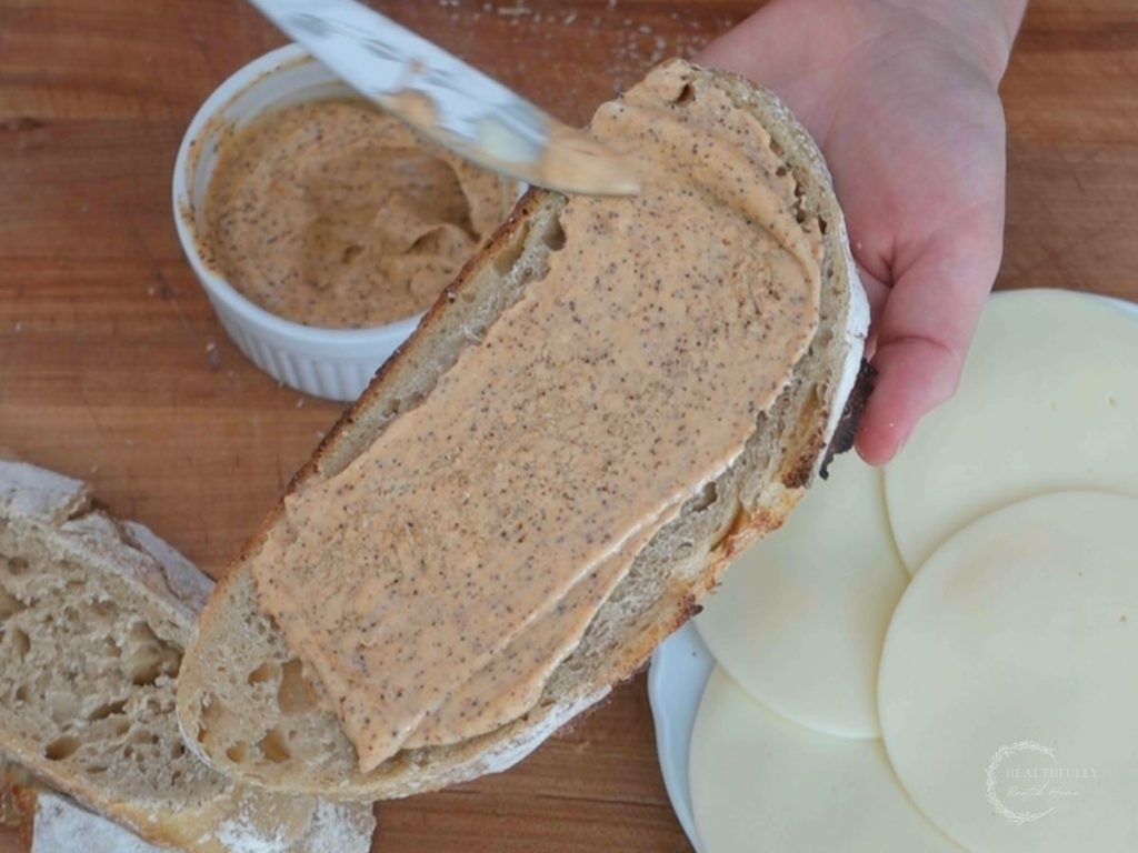 spreading ancho aioli over a slice of sourdough bread to make a grilled cheese sandwich