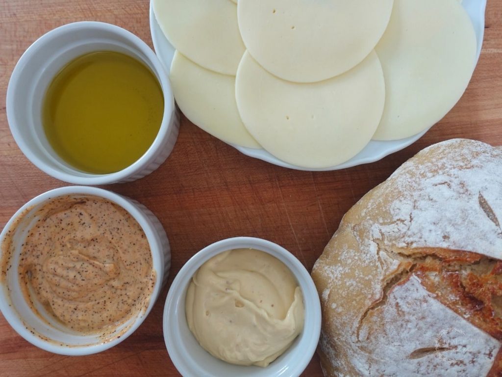 options for making a grilled cheese without butter with a plate of cheese and bowls with different fats for the grilled cheese and a loaf of bread