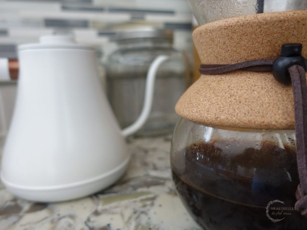 chemex hand drip coffee maker with a cork and tie with a white electric gooseneck kettle in the background