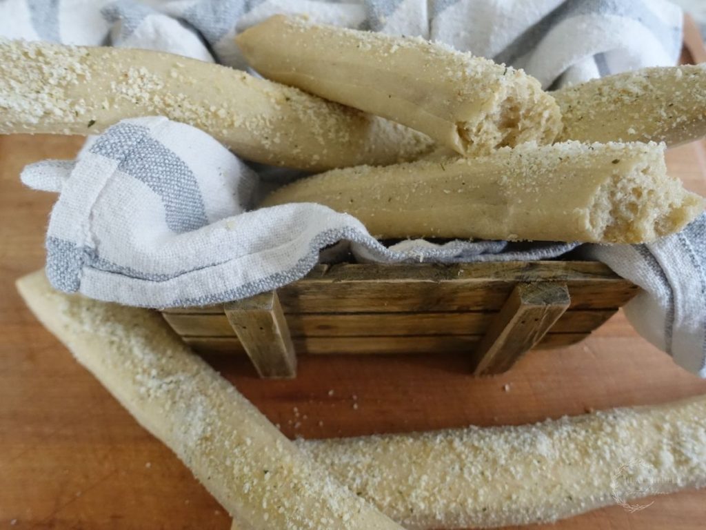 sourdough breadsticks in a tea towel lined basket with garlic parmesan topping with one broken in half so you can see how fluffy they are