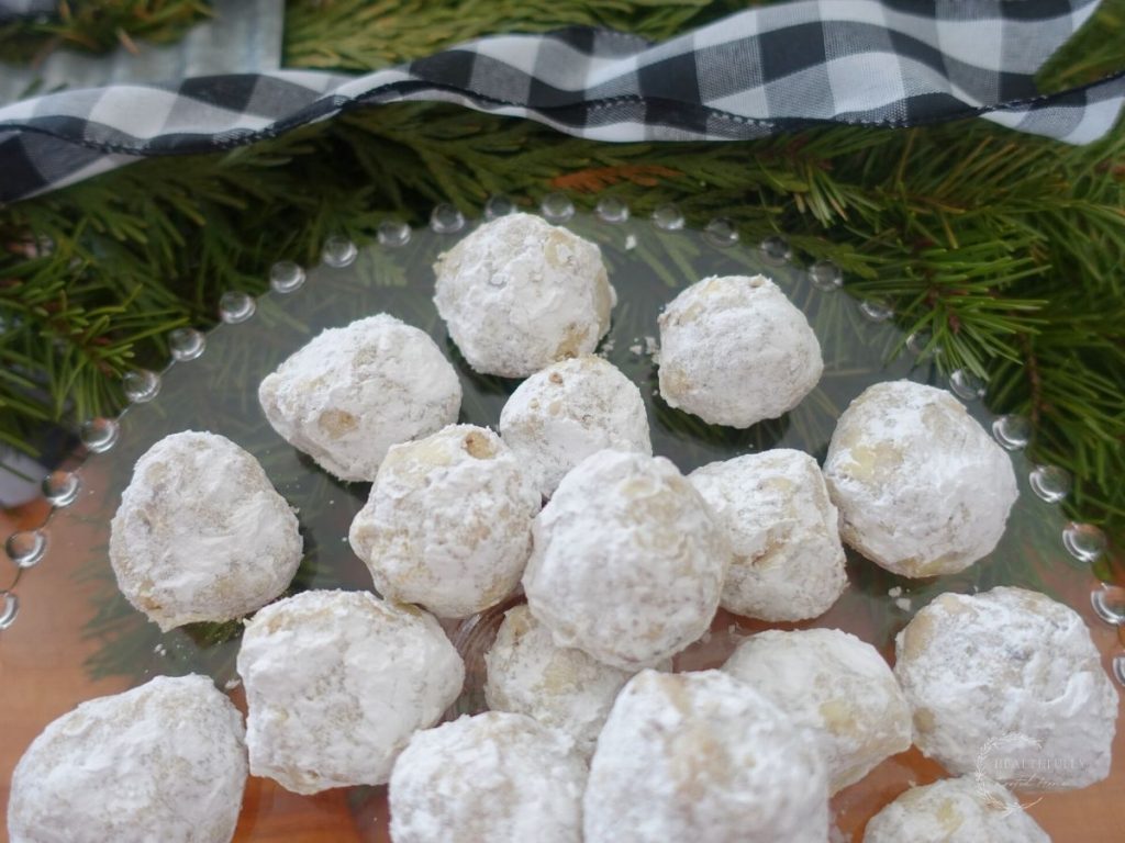 pecan meltaway cookies on a glass cake stand with fir tree branches in the background and a white and black checkered ribbon