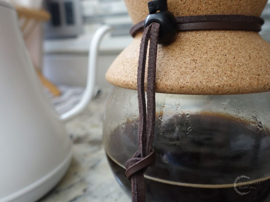 chemex hand drip coffee maker with cork and tie and a white electric gooseneck kettle in back