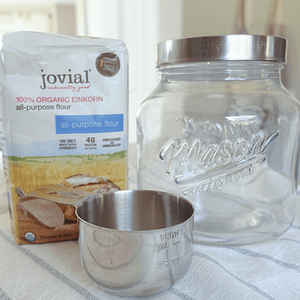 materials to make natural yeast jovial einkorn flour mason jar and measuring cup on top of tea towel
