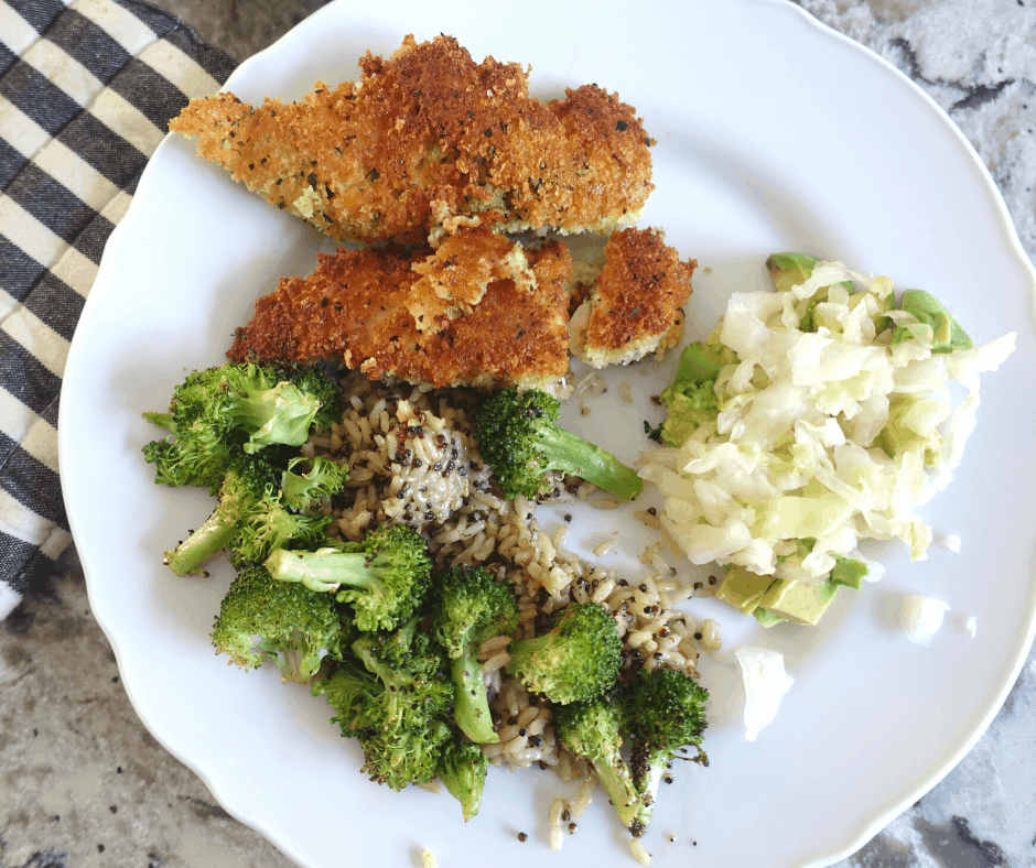 lacto fermented sauerkraut with avocado, broccoli, rice, and breaded chicken on a white plate with a striped hot pad next to it.