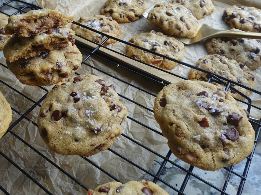 maple chocolate chip cookies on a cooling rack and a baking sheet some stacked on top eachother