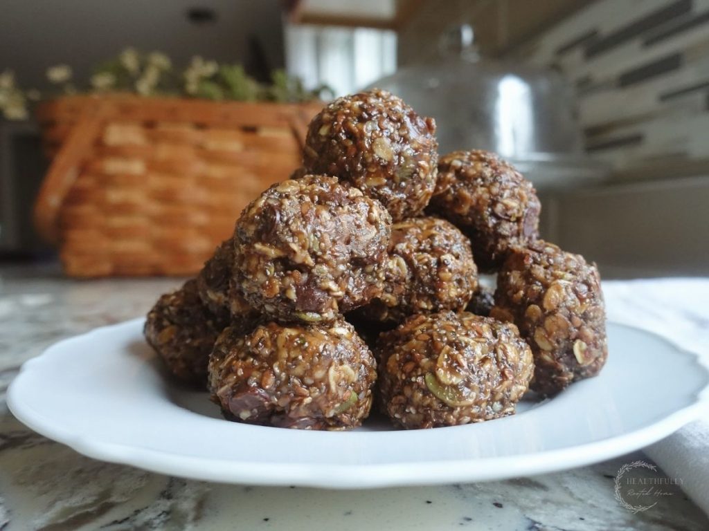 peanut butter bliss balls on a white plate with a brown basket in the background and a glass cake stand