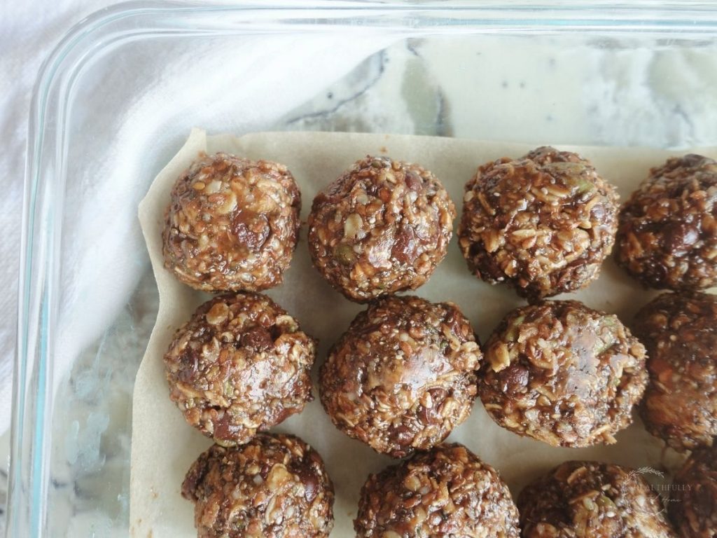 peanut butter bliss balls lined up in a storage container on top of parchment paper
