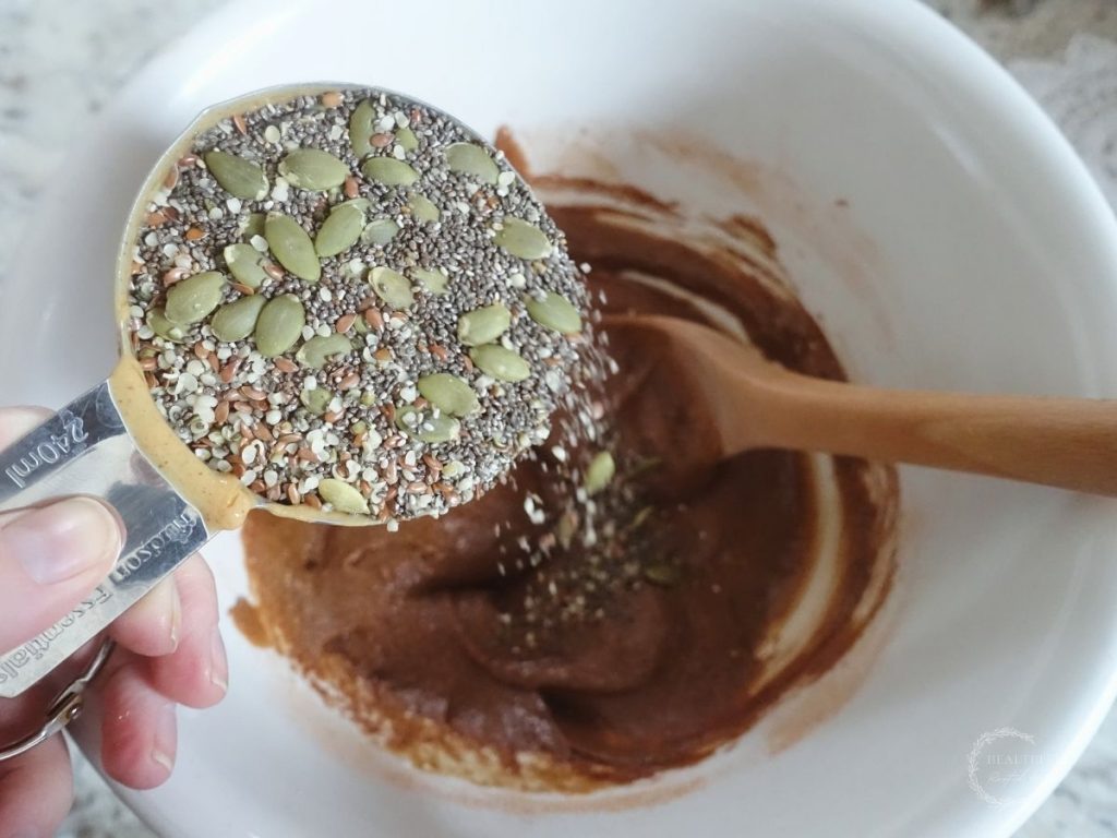 super seed blend in a stainless steel measuring cup being poured into a bowl with batter and a wooden spoon