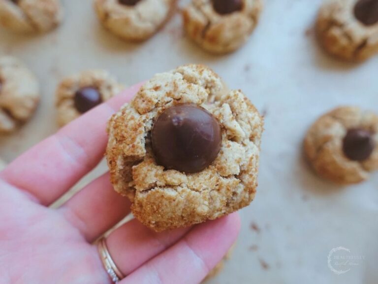 holding up a peanut butter kiss with a batch of peanut kisses in the background