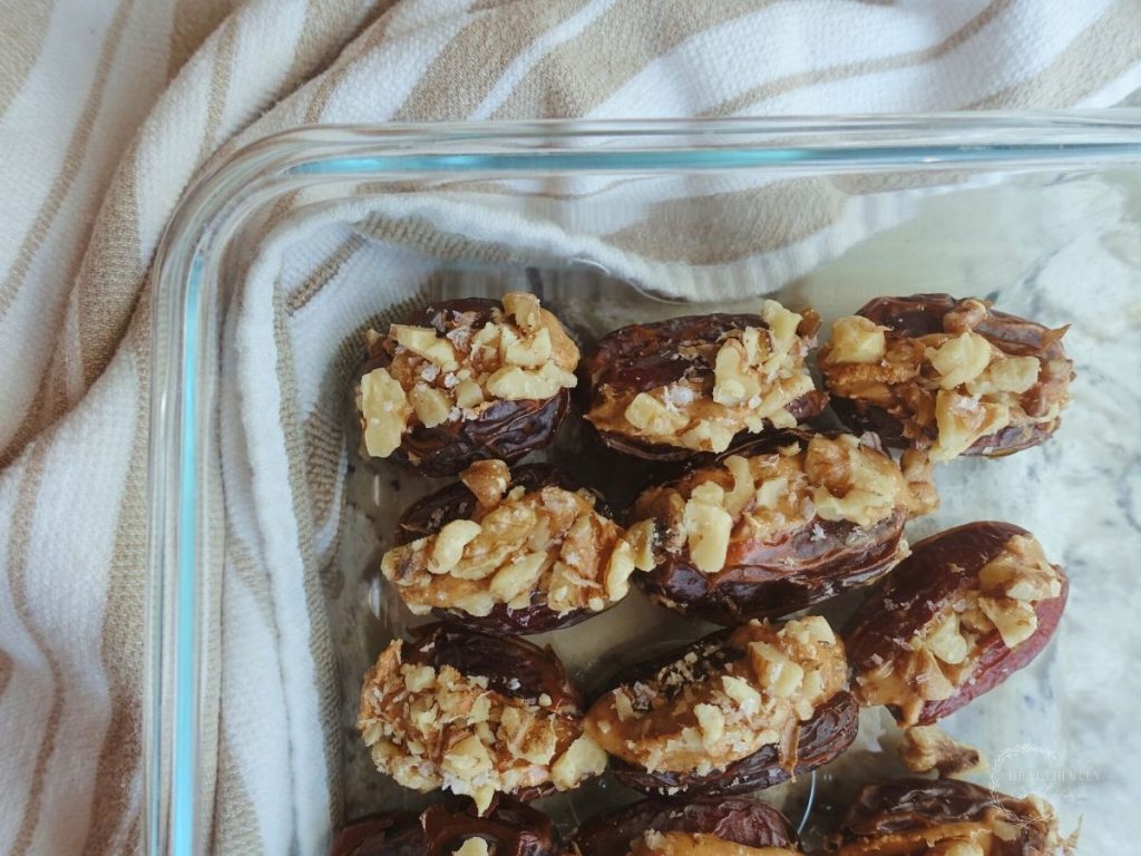peanut butter stuffed dates inside of a glass container with a white and brown striped tea towel in the background