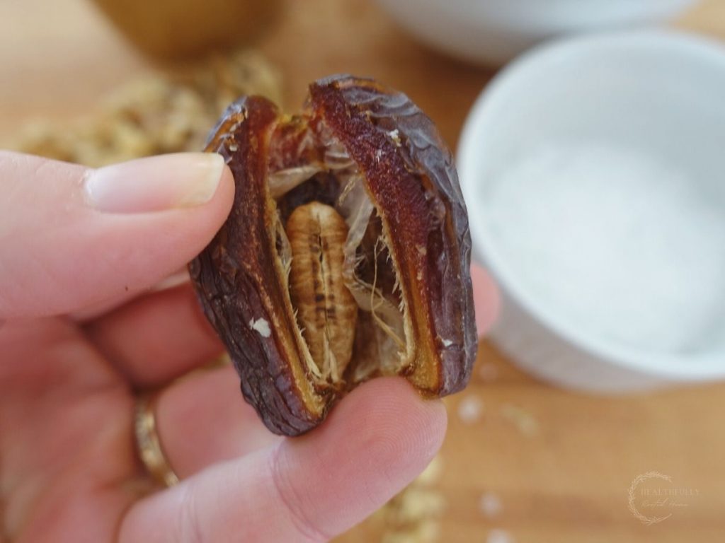 sliced in half date with pit exposed with a bowl of salt in the background