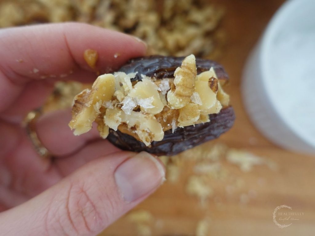 date stuffed with peanut butter and topped with walnuts and sea salt with a bunch of chopped dates and a bowl of sea salt in the background