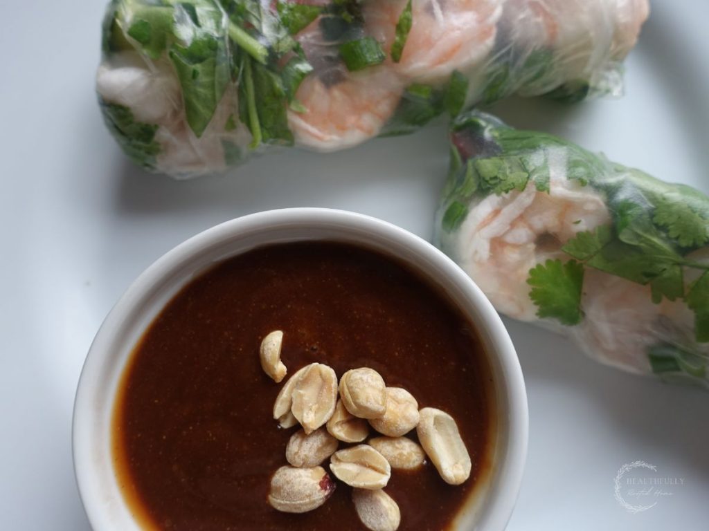 hoisin peanut sauce in a white bowl with chopped peanuts as the garnish and homemade spring rolls on the side