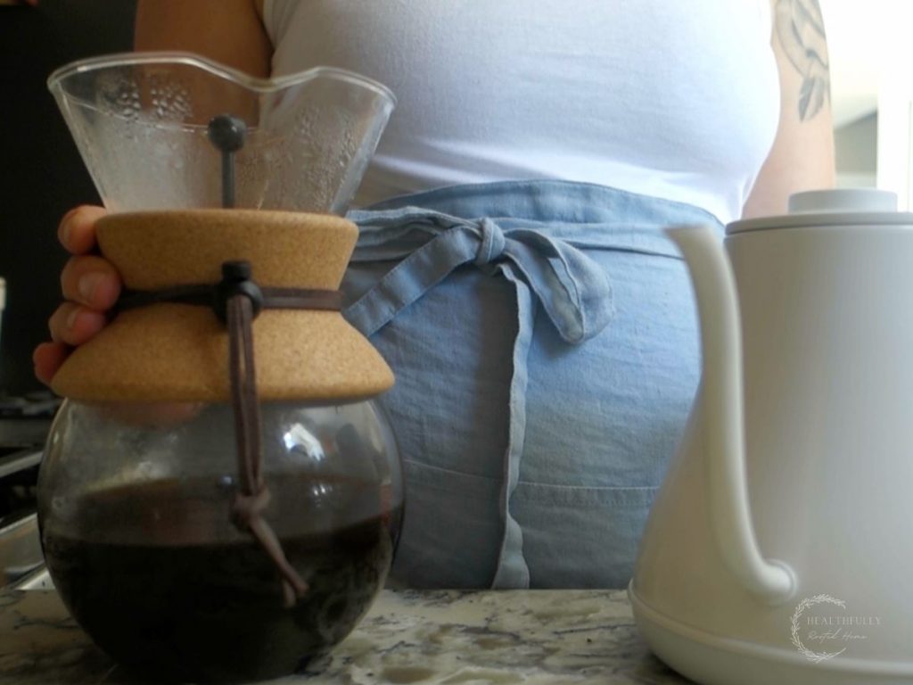 woman in apron using a chemex hand drip coffee maker with an electric gooseneck kettle to make pour over coffee