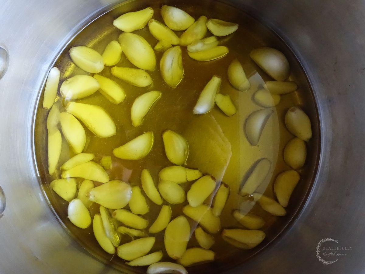 garlic cloves inside of a sauce pan covered in olive oil to make garlic confit