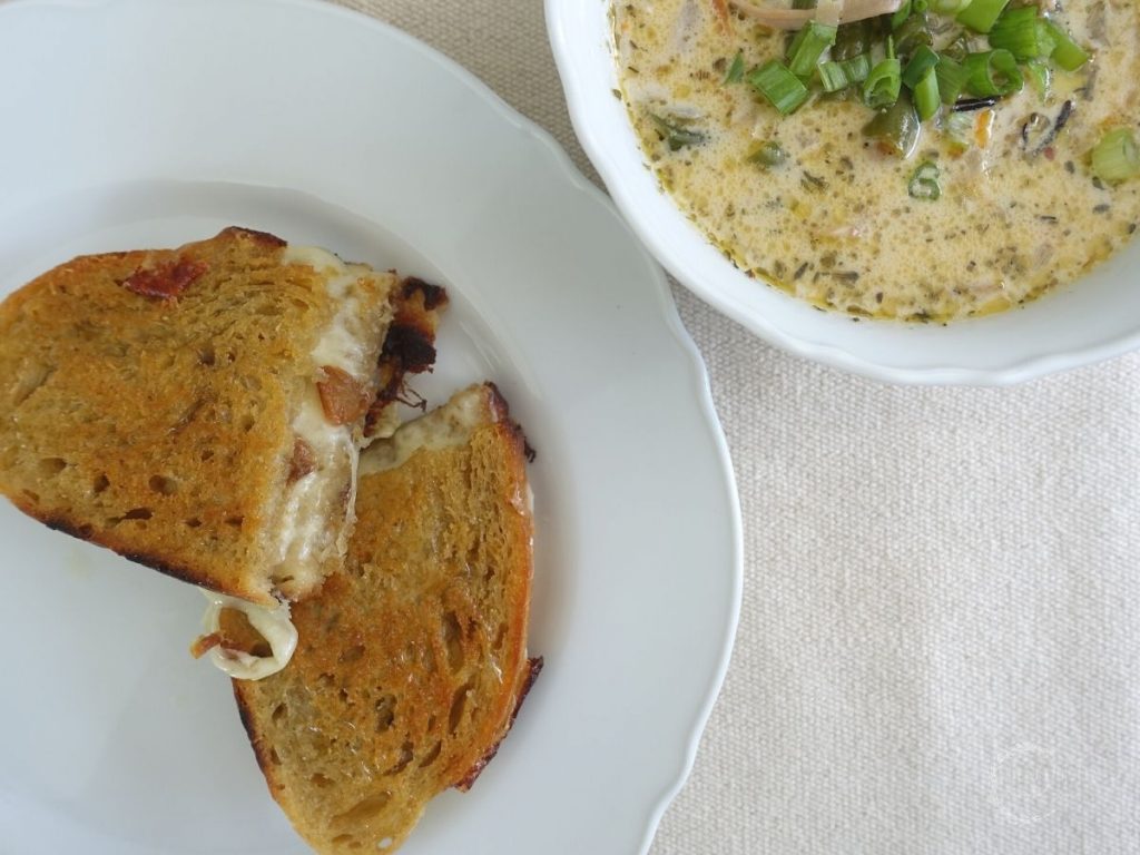 provolone grilled cheese cut in half and stacked on a white plate next to a bowl of soup