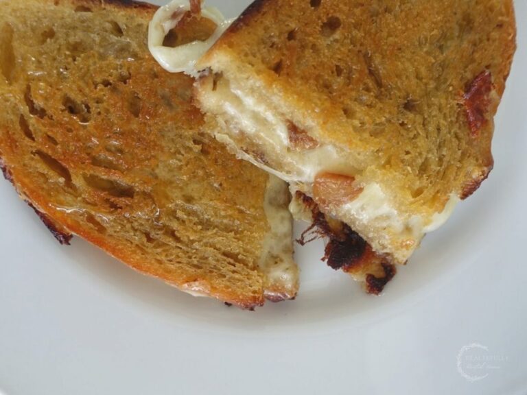 provolone grilled cheese sandwich with honey and garlic confit spread on homemade sourdough bread on a white plate with melted cheese dripping out