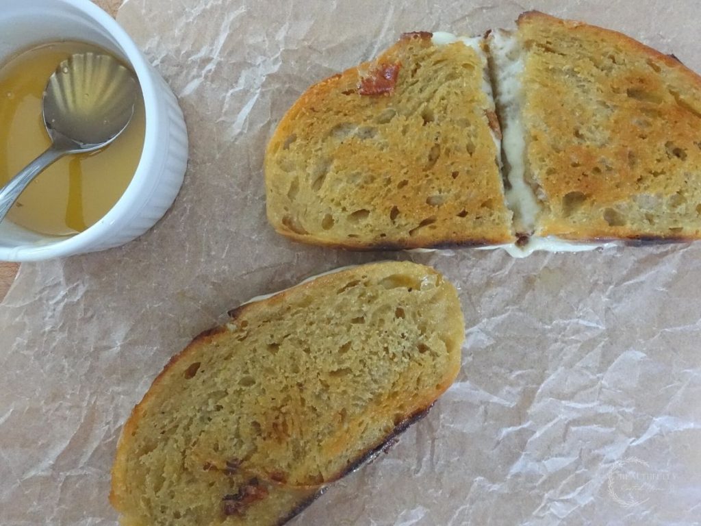 two provolone grilled cheese sandwiches after being fried sitting next to a jar of honey with a silver spoon in it