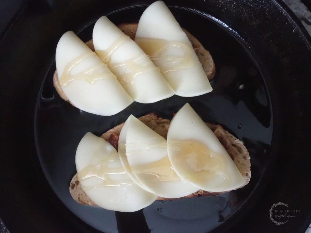 sourdough bread topped with provolone cheese and drizzled with honey inside of a cast iron skillet to make grilled cheese