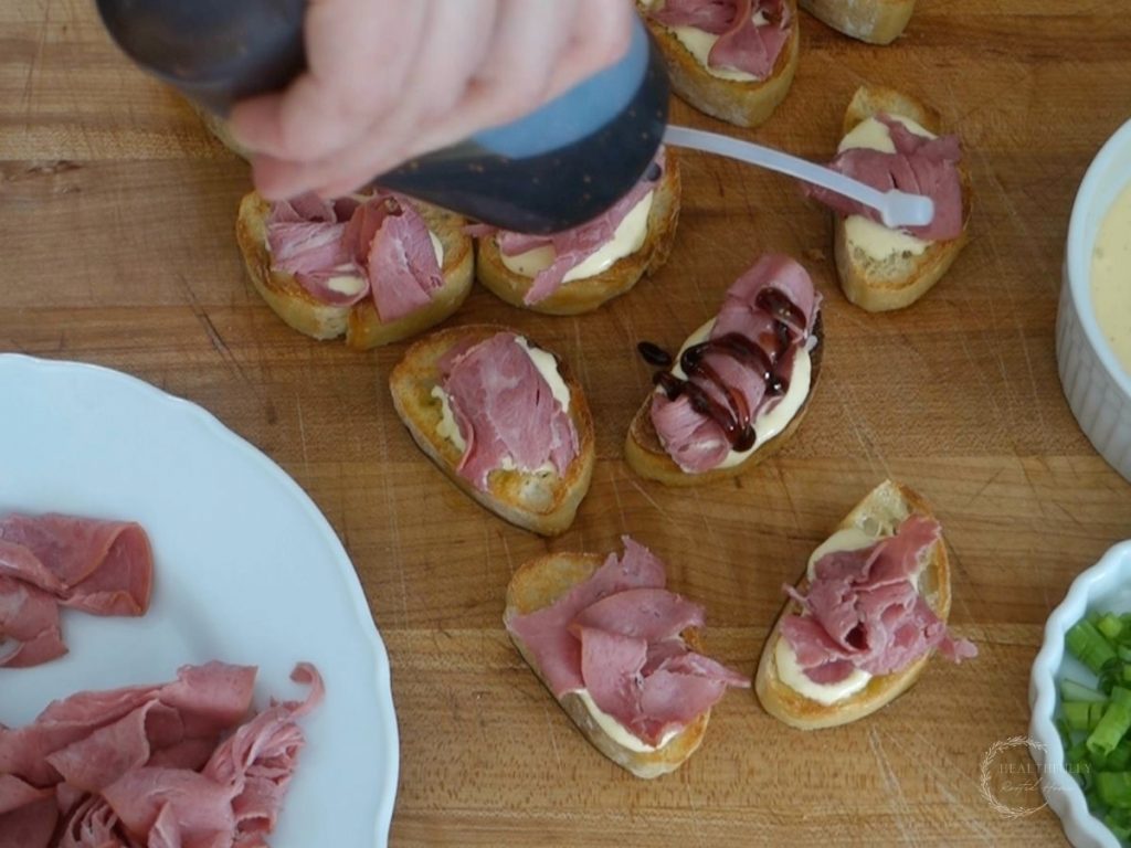 drizzling balsamic fig glaze overtop beef crostini slices using a squirt bottle