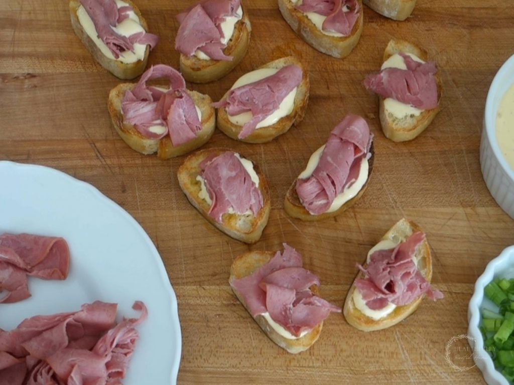 beef crostini slices next to a plate of roast beef on top of a wooden cutting board