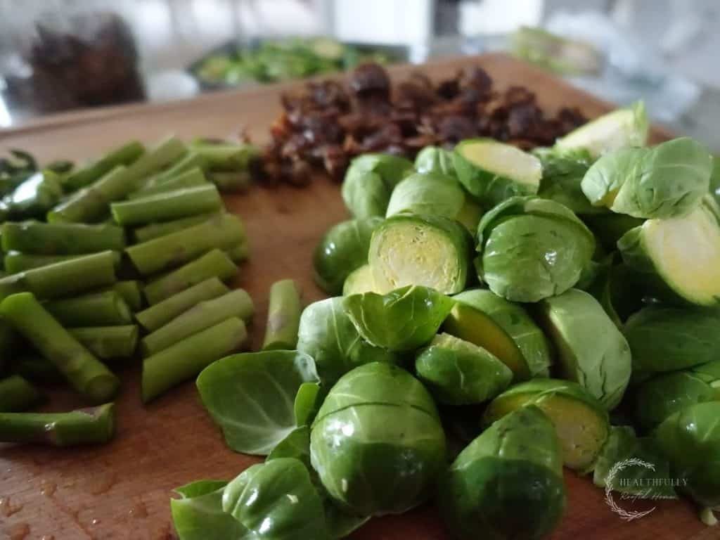 brussels sprouts halved asparagus chopped and dates diced on a wooden boos block cutting board