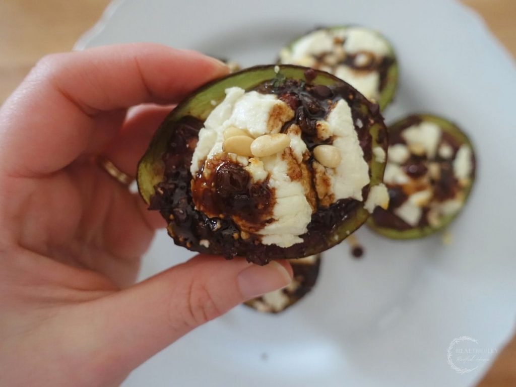 holding up a stuffed roasted avocado above a white plate